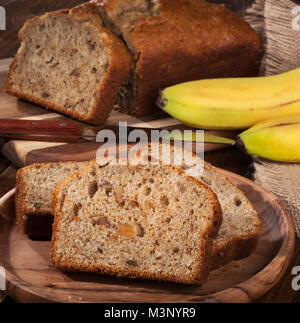 Slices of banana nut bread on a wooden plate with sliced loaf and bananas in background Stock Photo