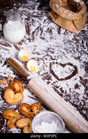 close-up view of heart symbol drawn in flour, rolling pin and ingredients for dough on table Stock Photo