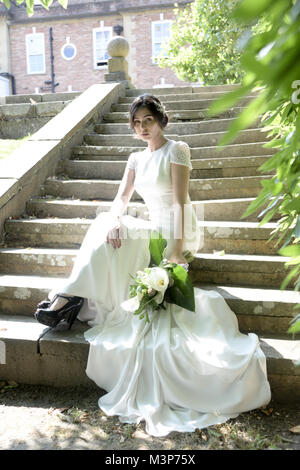 A beautiful dark haired bride wearing a fitted expensive Wedding Dress on a sunny day- brightly lit Stock Photo