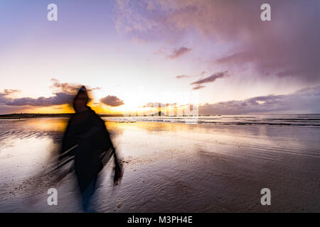 Picture of a ghostly / ghoulish figure on the beach at sunrise at Marazion ( result of a long exposure ) Stock Photo