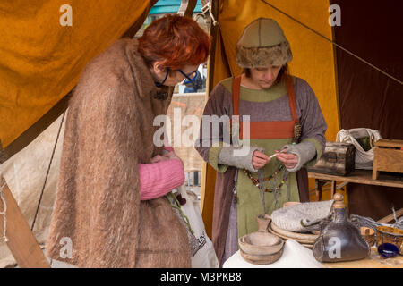 York, UK, 12th February 2018, Two women together, one dressed as a Viking, at the annual Jorvik Viking Festival. The lady on the right is taking part in a realistic re-enactment of life at a Viking market. She is demonstrating the art of knitting with a single needle (naalbinding) to a member of the public, who is clearly interested & watching closely. City centre of York, North Yorkshire, England, UK.  Credit: Ian Lamond/Alamy Live News Stock Photo