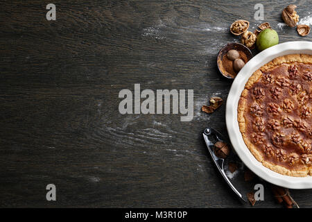 Traditional walnut pie with ingredients on dark wooden table Stock Photo