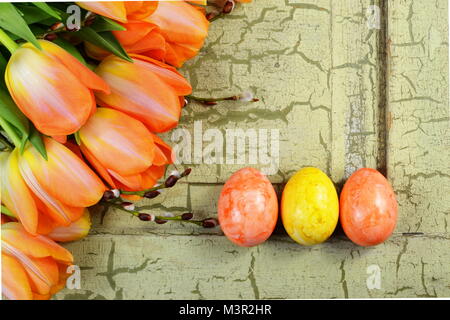 Orange and yellow easter eggs with orange tulips on a green vintage background . Stock Photo