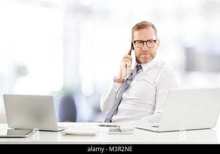 Portrait of financial assistant businessman using mobile phone and making call while working on laptop at the office. Stock Photo