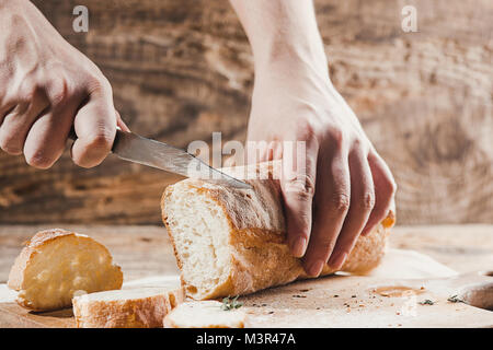 Whole grain bread put on kitchen wood plate with a chef holding gold knife for cut. Stock Photo