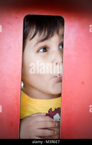 kid joking, Brunette boy putting funny faces in an outdoor park Stock Photo