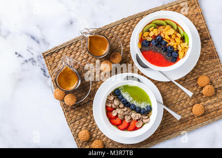 two bowls with different Smoothies from strawberries and kiwi, with Cereals for a healthy Breakfast and berries, chia seeds and coconut chips with fre Stock Photo