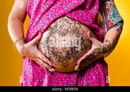 A color photo of a henna tatoo on a woman's pregnant belly, on yellow background. Stock Photo