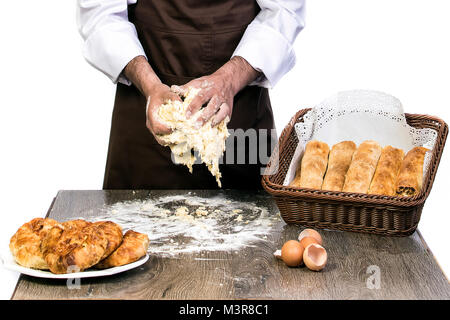 a man in an apron prepares the dough for baking, Cook model on a white background kneads dough on the table decorated with bakery products Stock Photo