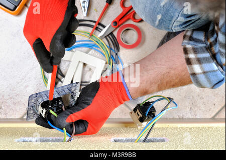 Electrician technician at work blocks the cable between the clamps of a socket in a residential electrical installation Stock Photo