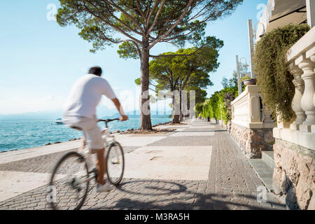 A man riding a bicycle along Garda Lake near Lazise town in Italy Stock Photo