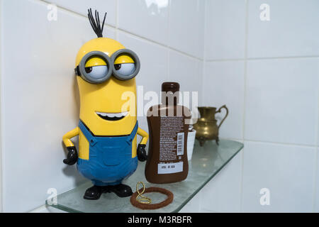 A  yellow and blue minion stands on a glass shelf in a bsthroom. Stock Photo