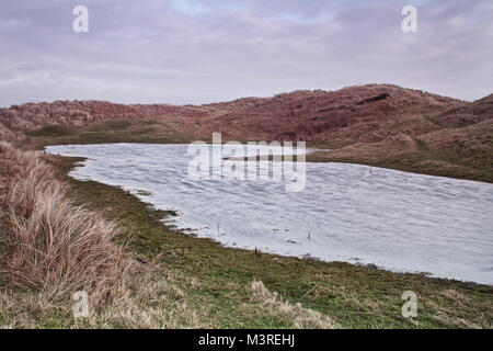 A picturesque pond on the nature reserve of South Walney, Walney Island, has no visiting wildlife on a cold winter day Stock Photo