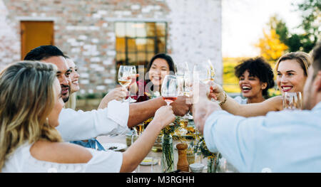 Group of men and women toasting wine at outdoor party. People having drinks during lunch at garden restaurant. Stock Photo