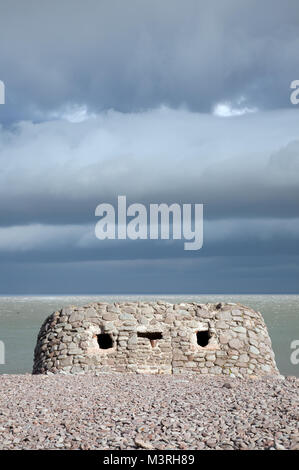 A World War II pillbox on the beach at Porlock Weir, Somerset, England, with dark, menacing clouds in the background. Stock Photo