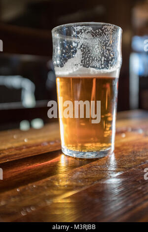 Half full pint of beer on pub table Stock Photo
