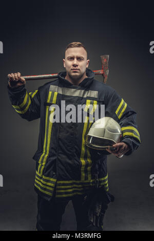 Firefighter costume holding helmet and recue red axe. Stock Photo
