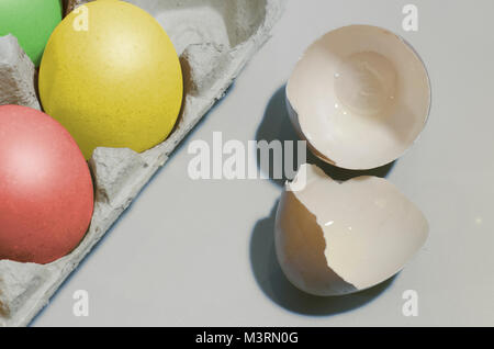 closeup shot with colorful cardboard container with chicken eggs, one is broken, four eggs painted in different colors. Easter concept Stock Photo