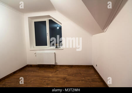 Empty small room with wooden oak parquet floor, newly painted white walls, heating radiator and a window. Attic room. Stock Photo