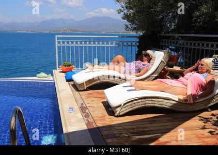 28TH JULY 2017, SOVALYE ISLAND,TURKEY:Two english ladies relaxing on sunbeds next to an infinity pool while on vacation on sovalye island, turkey Stock Photo