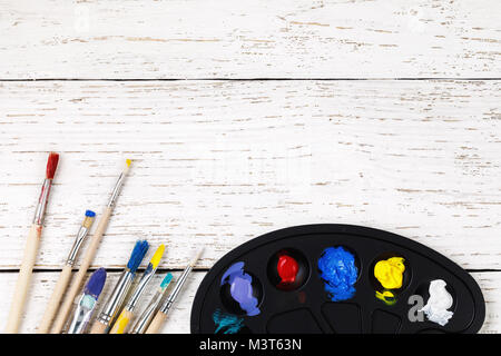 Artistic accessories: a palette with paints and tassels for drawing on a wooden table with space for text, top view Stock Photo