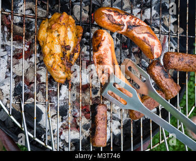 View from above onto a variety of roast meat and sausages on a barbecue grill rack on charcoal embers. Stock Photo