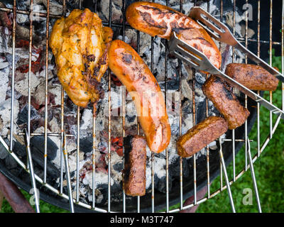 View from above onto a variety of roast meat and sausages on a barbecue grill rack on charcoal embers. Stock Photo