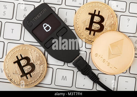 Black Trezor hardware wallet for cryptocurrency with golden bitcoin with black reflection and ethereum coins on keyboard Stock Photo
