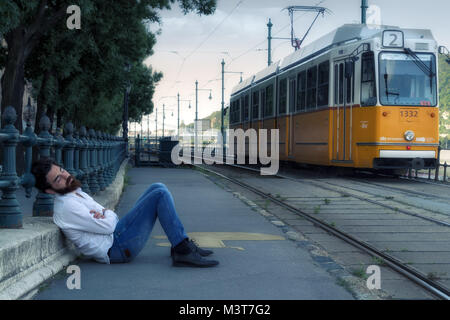 Young man is sleeping on the ground at tram stop Stock Photo