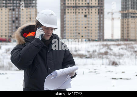 Architect, engineer, project manager or Senior engineer man talking on CB phone to building in the city with a blank plan as for construction. Soft fo Stock Photo
