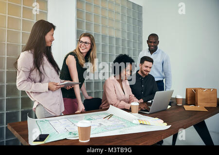 Diverse group of business colleagues smiling and having a discussion while working together at a desk in a modern office Stock Photo