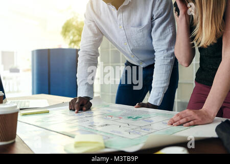 Closeup of two architects standing in a modern office leaning over a desk discussing a building design together Stock Photo