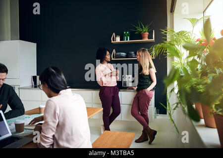 Two businesswomen smiling and talking together while taking a break in a modern office Stock Photo