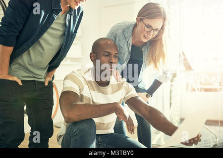 Three diverse young business colleagues reading a document together while working in a modern office Stock Photo