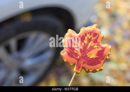 Tasty handmade cookie in the form of a maple leaf on the background of a car wheel on the street in the fall Stock Photo