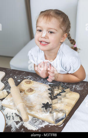 The process of cooking dumplings at home. Funny little girl smiling while sitting in the kitchen Stock Photo