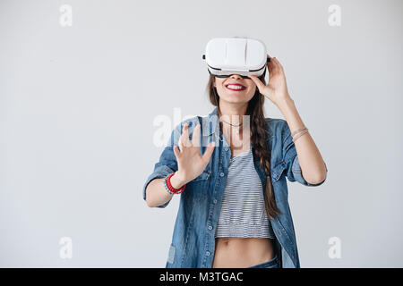 Happy loughing young woman getting experience using VR glasses on white background much gesticulating hands. Impressed girl touching hair while using  Stock Photo