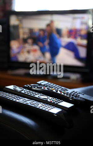 A range of remote controls for television, satellite, DVD and sound system, on the arm of a chair, in Peterborough, Cambridgeshire, on February 12, 20 Stock Photo