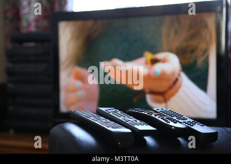 A range of remote controls for television, satellite, DVD and sound system, on the arm of a chair, in Peterborough, Cambridgeshire, on February 12, 20 Stock Photo