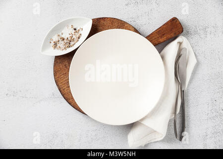 empty plate and cutlery on a wooden cutting board. a fork, a knife and a salt bowl with a pepper shaker. on white stone background, napkin. the table  Stock Photo