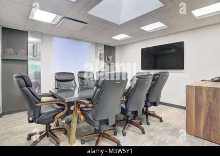 A small, eight-person corporate meeting room for company presentations with two screens, black leather office chairs and skylight in ceiling. Stock Photo