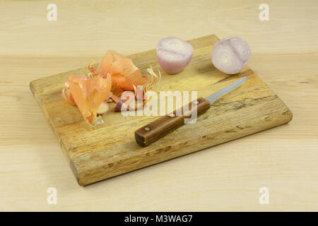 Raw shallot halves, skin, and knife on wooden cutting board on wood table Stock Photo