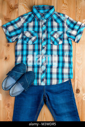 shoes, checkered blue shirt and jeans for a boy set on a wooden floor top view Stock Photo