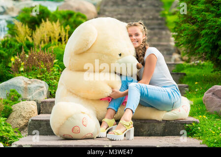 20 year old beautiful woman with a big teddy bear in the park on the stairs Stock Photo