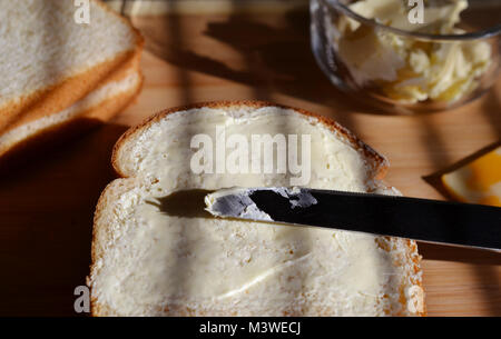 White bread with Mayo on it shown open face style with silver knife across it. Butter in glass dish and white bread also shown. Shadows. Stock Photo