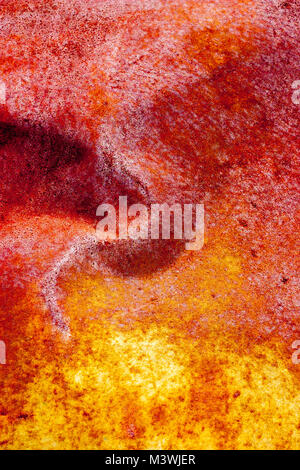 Vivid red and yellow colors produced by the oxidization, rusting, of a dented, metal sheet. Stock Photo