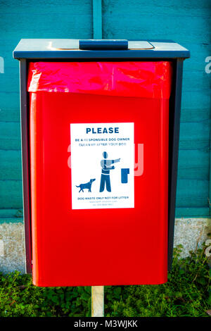 Bright red bin situated outside for dog waste, with a label reading: “Please be a responsible dog owner. Clean up after your dog.” England, UK. Stock Photo