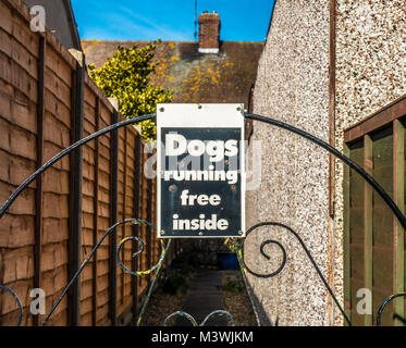 Warning sign / notice at the rear of a house, prominently displayed on an ornate metal gate, “Dogs running free inside”. England, UK. Stock Photo