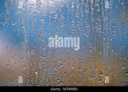 Background of raindrops running down a glass window isolated against soft, blue and tan colors. Stock Photo