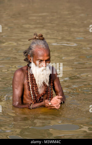 India. Varanasi (Benares). The ghats. Hindu pilgrims bathing and worshipping and to wash away their sins in the Ganges River. Hindu holy man (Sadhu). Stock Photo